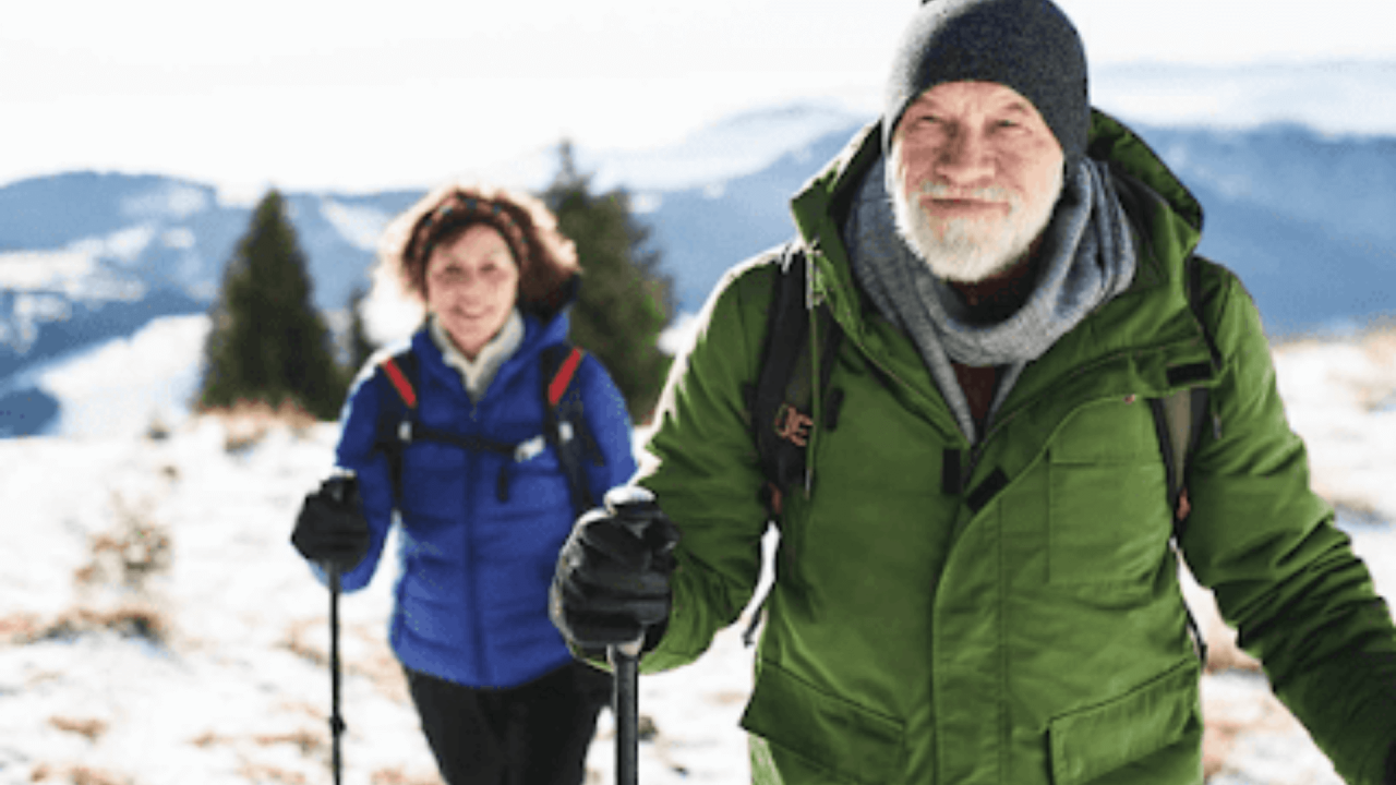 Hombre y mujer mayores caminando por la nieve con bastones en una imagen de invierno